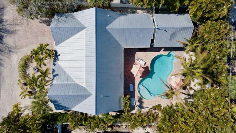 Stunning beachfront property featuring a crystal-clear pool surrounded by swaying palms and pristine sandy shores.