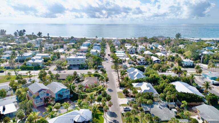 Aerial view of a tropical coastal neighborhood with colorful homes nestled among palm trees, just steps from pristine beaches.