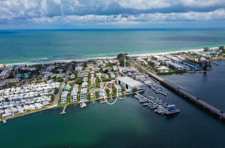Stunning aerial view showcases waterfront properties nestled between pristine beaches and protected marina, offering the perfect coastal getaway location.