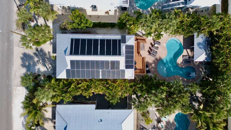 Aerial view of a tropical vacation rental with solar panels, swimming pool, and lush palm trees creating a private paradise.