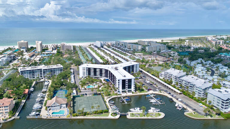 Aerial view of a waterfront resort property with expansive grounds, nestled between tranquil waters and lush tropical landscaping.