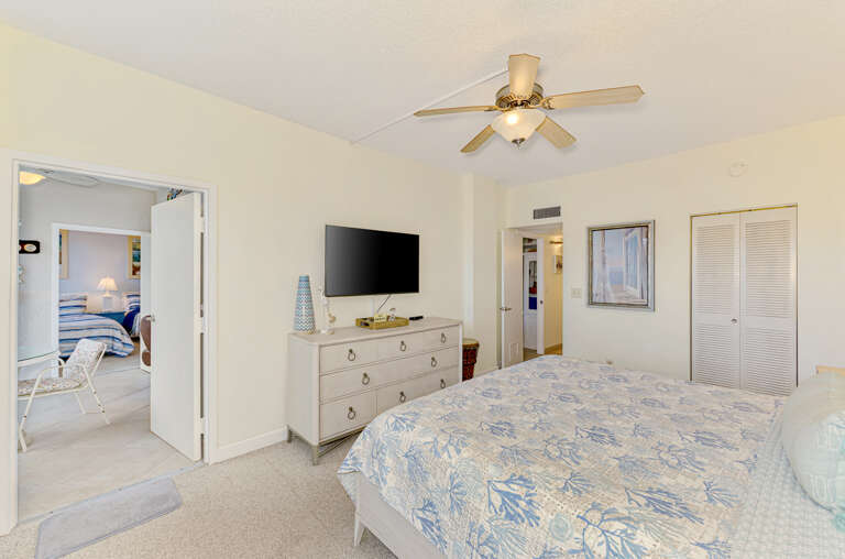 Unwind in your spacious bedroom with coastal-themed bedding, ceiling fan for comfort, flat-screen TV, and plenty of storage space.