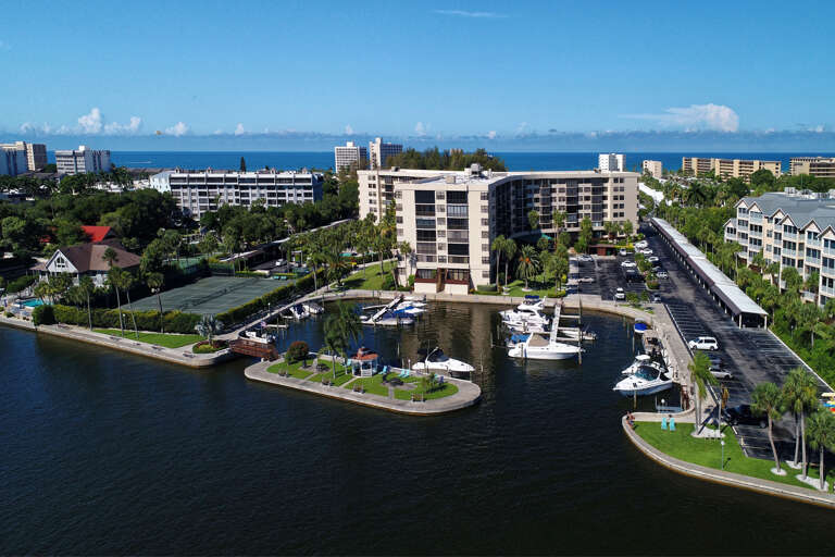 Waterfront community featuring marina access, resort-style buildings, and tropical landscaping near pristine coastal waters.