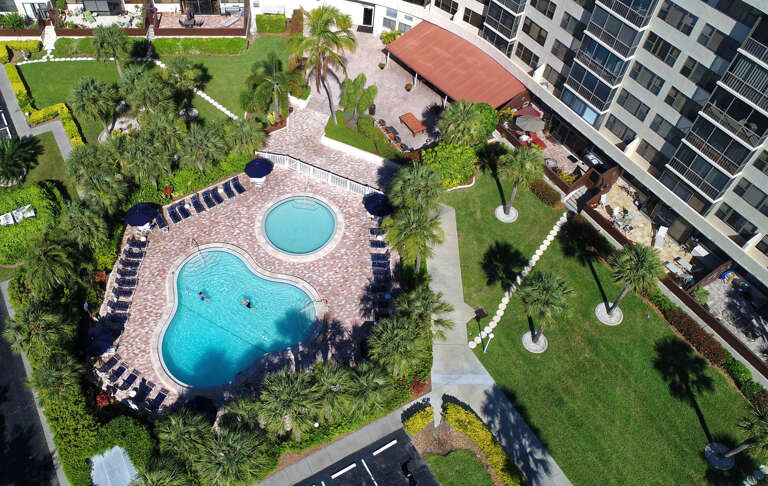 Aerial view showcasing the resort-style pool area with tropical landscaping, surrounded by modern apartment buildings and lush green spaces.