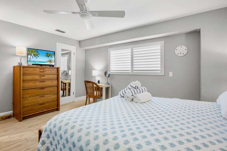 Drift off in your coastal-inspired bedroom featuring soft linens, warm wood furniture, and a peaceful ceiling fan breeze.