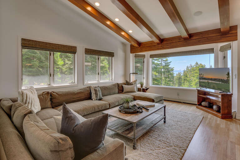 Spacious Living Room With Large Windows, Lush Views, And Timber Beams