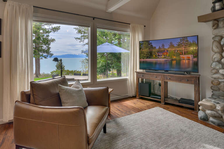Lakeside Living Area With Large Windows, View Of Serene Waters, Plush Sofa, And Stone Fireplace