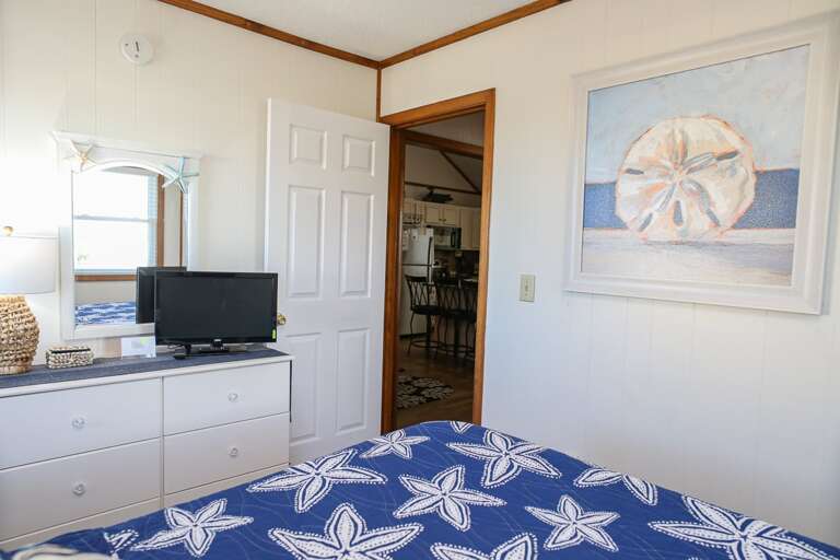 Bedroom With Starfish-patterned Bedspread, Dresser, TV, Mirror, And Connecting Room View