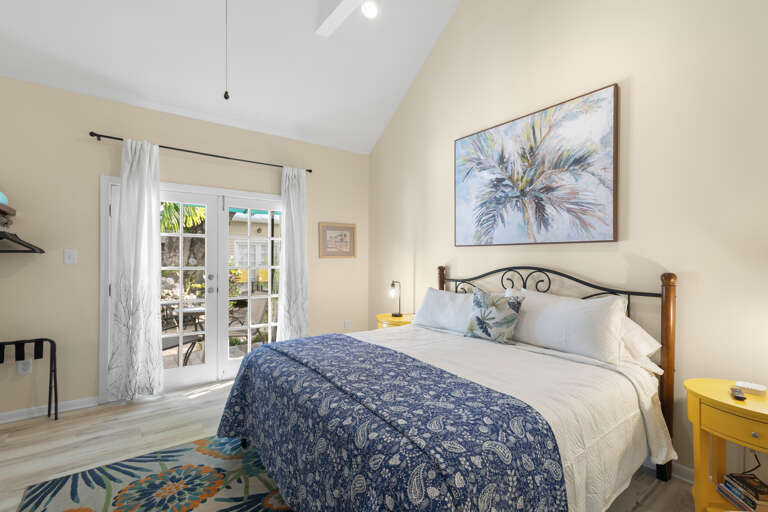 Step into your bright, airy bedroom with vaulted ceilings and French doors opening to a private patio. The tropical artwork and cheerful blue and yellow accents set a relaxed coastal mood.