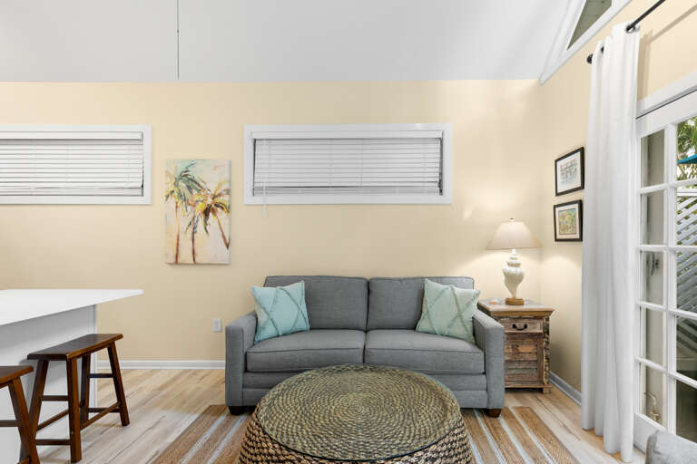Unwind in your cozy living area with a comfy sofa, calming coastal touches, and natural light filtering through the windows to create a serene, beachy atmosphere.