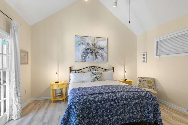 Slip into this airy bedroom with soaring ceilings and coastal charm. Your bed awaits beneath soft linens and island-inspired art, while cheerful pops of yellow brighten the space.