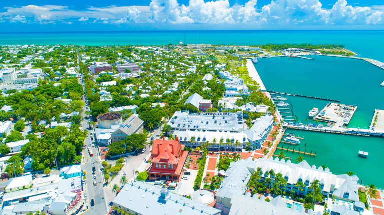 Aerial view of a vibrant coastal town with a marina, historic buildings, and lush tropical vegetation surrounded by turquoise waters.