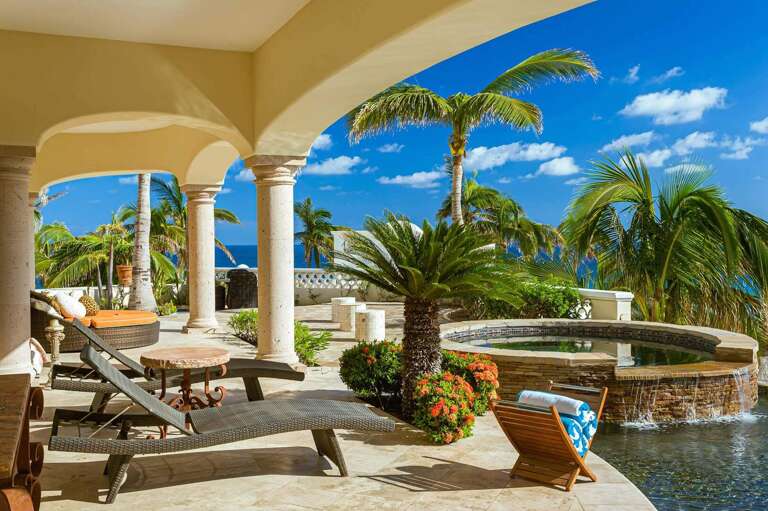 Sunlit Seaside Scene With A Spacious Terrace, Towering Palms, And Tranquil Turquoise Waters