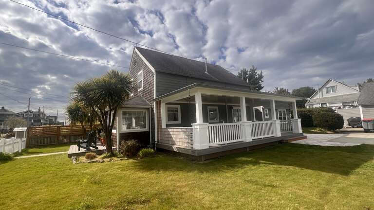 Charming coastal cottage with wraparound porch and lush lawn in peaceful residential neighborhood.