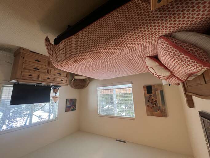 Wake up in a cozy bedroom where charming red patterned bedding meets natural light streaming through bright windows. Your peaceful retreat awaits with warm wood tones and a ceiling fan overhead.