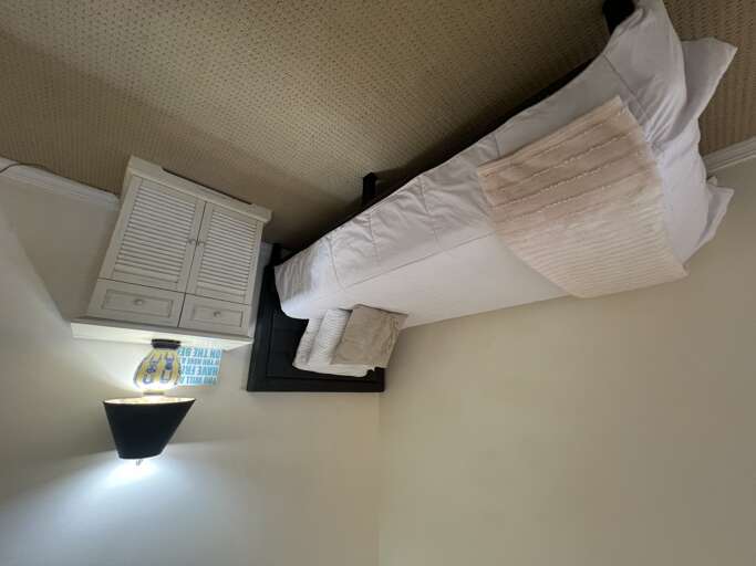 Your cozy bedroom features a comfortable bed with crisp white linens and extra pillows, plus storage and a desk workspace. Everything you need for a restful, productive stay.