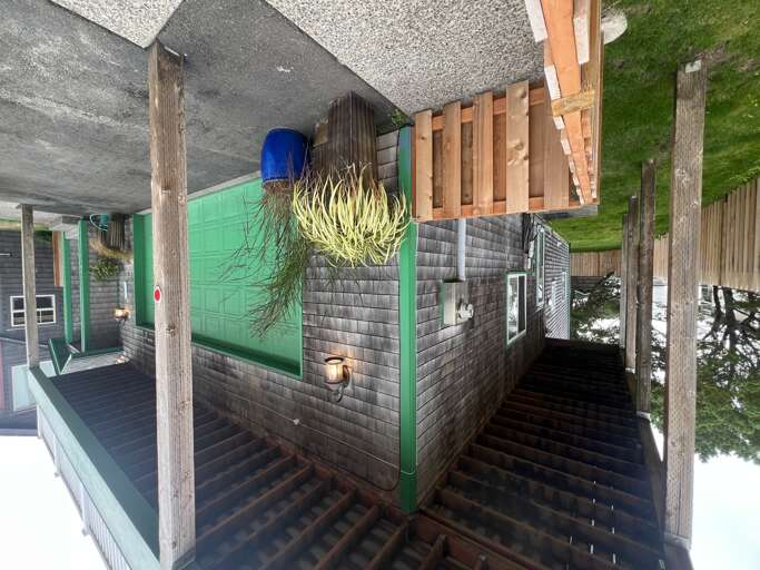 Aerial overview of the property featuring charming rustic architecture with weathered wood posts, distinctive green accents, and a spacious deck surrounded by lush greenery and natural landscape.