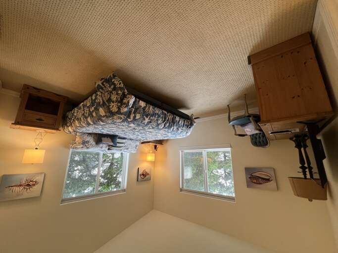 Your cozy bedroom features a plush bed with decorative linens, warm lighting, and peaceful tree views through dual windows, creating a restful retreat for your stay.