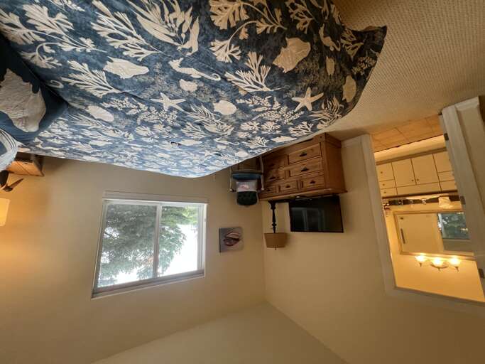 Drift off beneath a stunning ocean-inspired ceiling mural in your cozy bedroom, with a dresser, TV, and bright natural light to greet you each morning.