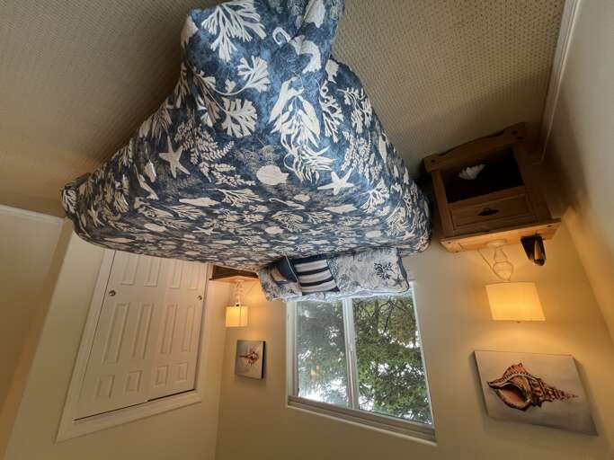 Slip into crisp, coastal-themed linens and wake to soft natural light filtering through the window, framing peaceful garden views. Your restful retreat awaits with thoughtful decor and cozy touches.