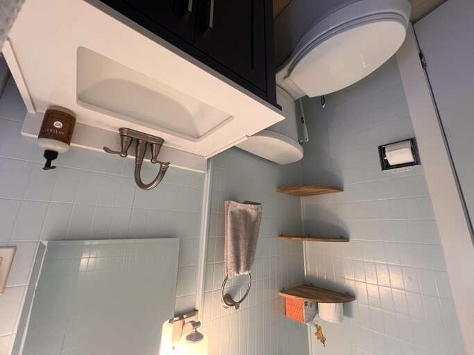 Your private bathroom features soft tiling, open shelving for your essentials, and a clean overhead shower—designed for comfort and ease during your stay.