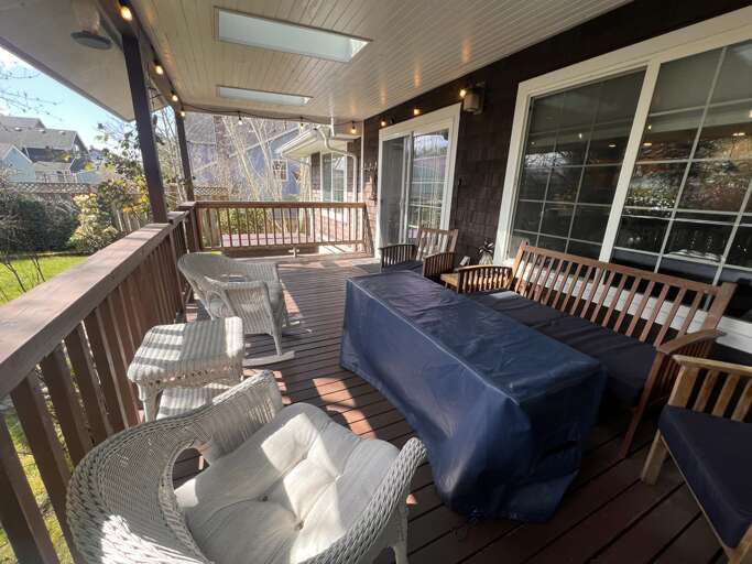 Relax on your private covered deck with skylights and string lighting, offering dining space and wicker seating overlooking a quiet neighborhood setting.