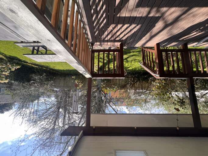 The property exterior features a covered wooden deck overlooking a peaceful river, surrounded by lush greenery and natural landscape.