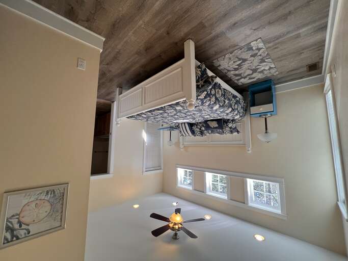 Your cozy bedroom features a plush bed with coastal blue and white linens, rustic wood ceiling, and natural light streaming through bright windowsâyour perfect retreat after a day of adventure.