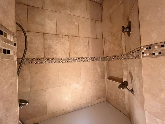 Elegant walk-in shower features mosaic tile detailing and dual showerheads for your ultimate relaxation after a day exploring the area.