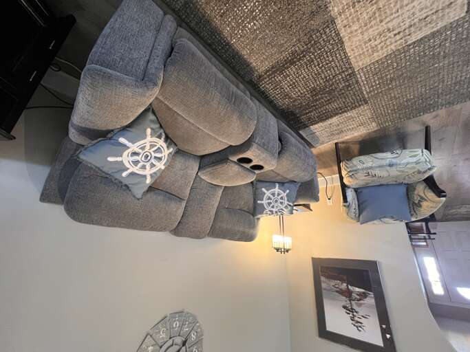Unwind on plush sectional seating adorned with nautical-themed pillows. The cozy living area features coastal dÃ©cor, soft lighting, and a welcoming ambiance perfect for your relaxation.