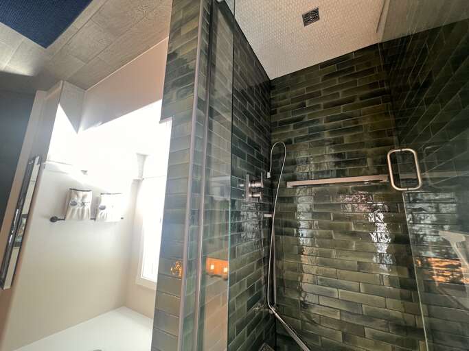 Step into your stylish walk-in shower, where glossy emerald tiles and a sleek rainfall showerhead create a spa-like retreat. The modern fixtures and rich texture invite you to unwind in comfort.