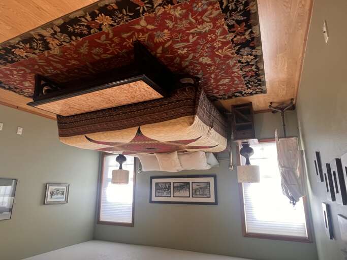 Look up and discover the unique artistry overhead—an intricate woven rug suspended from the ceiling creates an unexpected canopy, while decorative textiles and carved woodwork frame this one-of-a-kind space.