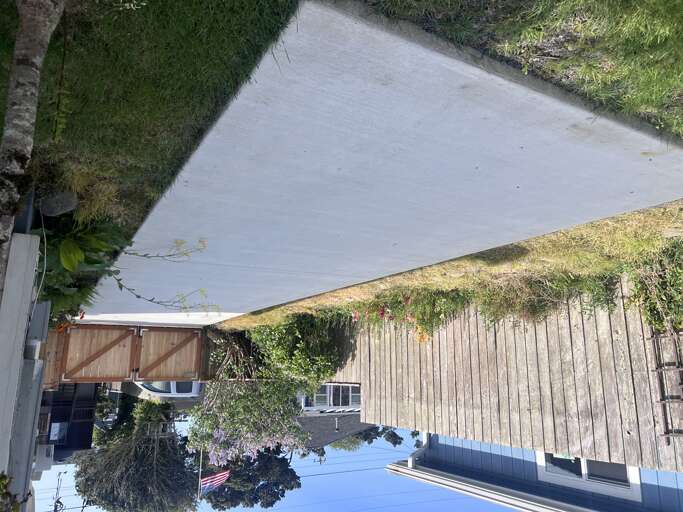 Aerial view of the property showing the backyard layout with grassy lawn, patio area, wooden deck, and private outdoor spaces bordered by trees.