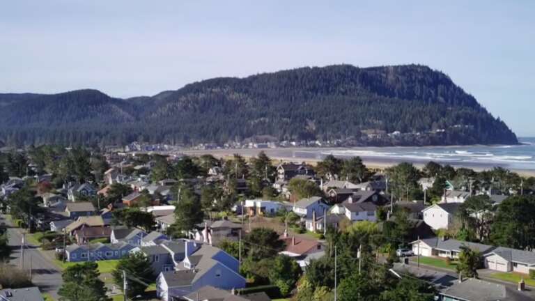 A scenic coastal town nestled between forested mountains and sandy beach, offering a peaceful retreat near natural beauty.