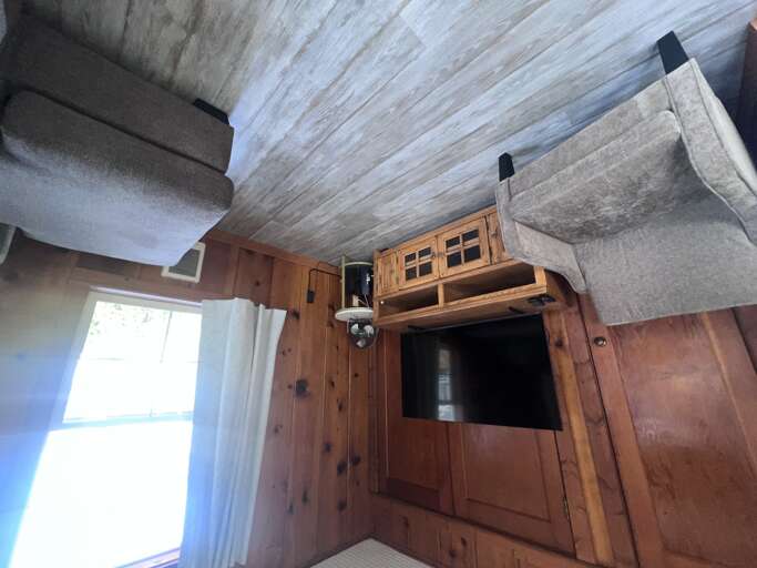 Cozy bedroom with warm wood paneling, a comfortable bed, TV entertainment center, and beach views just beyond your windowâyour perfect seaside retreat.