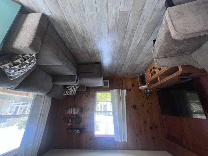 Your cozy living room features rustic wood-paneled ceilings, plush gray seating, and natural light streaming through the windows, creating a warm retreat for relaxation.