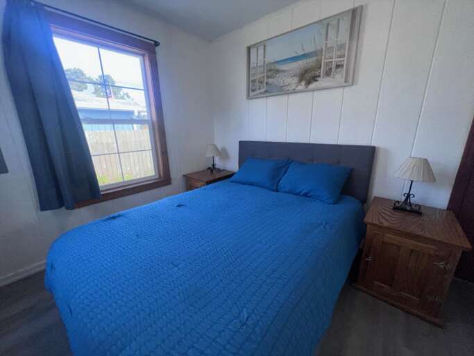 Unwind in your peaceful coastal bedroom with soft white walls, calming blue bedding, and serene beach artwork that invites restful sleep after your seaside adventures.
