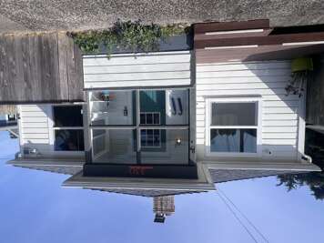 White cottage with dark trim and welcoming entrance flanked by large windows, situated in a peaceful residential area.