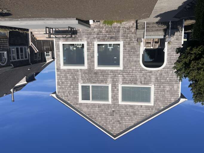 Modern beach house exterior featuring clean architectural lines and natural shingle siding, located in a quiet residential neighborhood just steps from the shore.