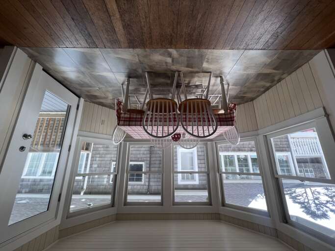 Step into your sunlit porch with charming rustic wood ceilings and abundant windows that frame the outdoors. Cozy seating awaits above, creating a peaceful nook to unwind and soak in natural light throughout your stay.