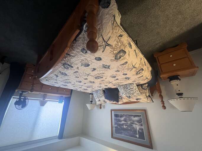 Your cozy bedroom features a classic wood-frame bed dressed in coastal-inspired linens, warm wood furnishings, and soft natural light streaming through the window to welcome restful mornings.
