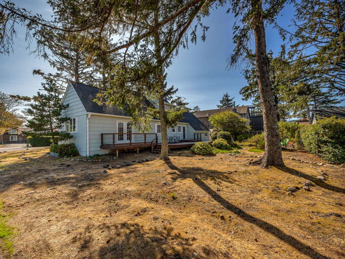 Charming coastal cottage with deck nestled among mature trees, offering a peaceful retreat in a quiet neighborhood setting.