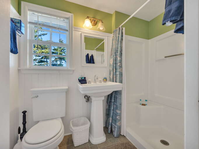 Your private bathroom features a bright window with tree views, a pedestal sink, walk-in shower, and fresh towels ready for your arrival—a clean, welcoming space to refresh after your adventures.