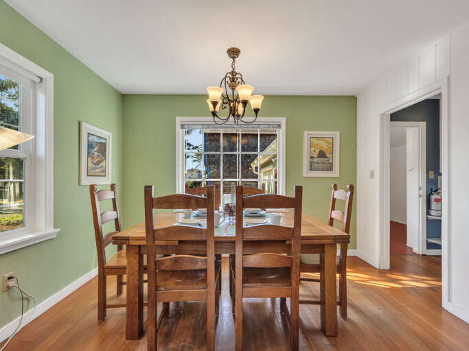 Gather around the farmhouse-style dining table, where warm wood tones and soft sage walls create an inviting space for shared meals and conversation beneath an elegant chandelier.