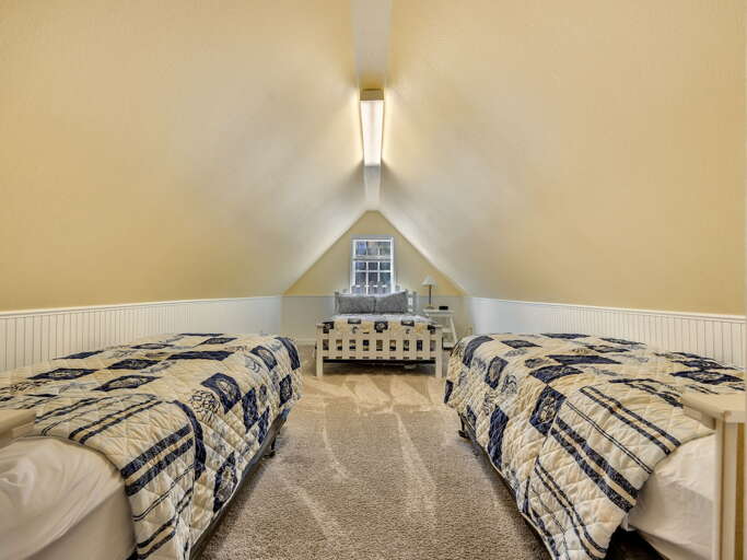 Cozy loft bedroom featuring three beds with cheerful blue and cream quilts, perfect for family gatherings or group getaways under vaulted ceilings.