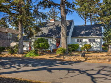 A charming coastal cottage nestled among towering pines, with mature landscaping and garage parking for guest convenience in a peaceful neighborhood.