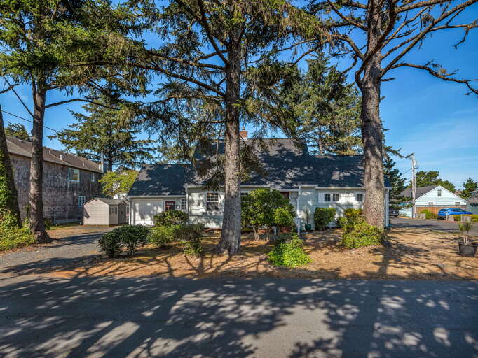 A charming coastal cottage nestled beneath towering evergreens, offering peaceful seaside living with nearby beach access and neighborhood charm.