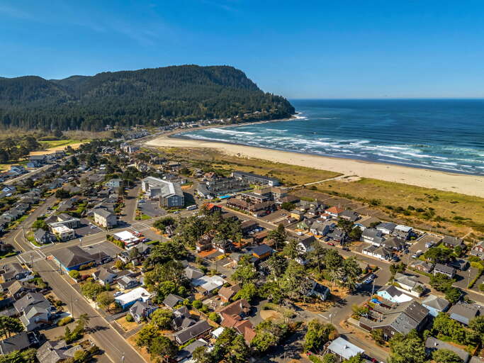 A scenic coastal town nestled between forested mountains and a pristine sandy beach, offering easy access to both natural beauty and local charm.