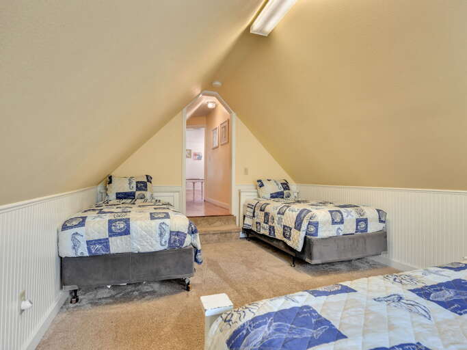 Your cozy attic bedroom features three comfy beds with nautical-themed linens, perfect for a peaceful night's rest under warm, sloping ceilings.