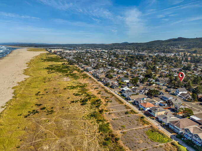 This coastal town offers a prime location nestled between wide sandy beaches and rolling hillsides, with the property marker identifying its proximity to the oceanfront.